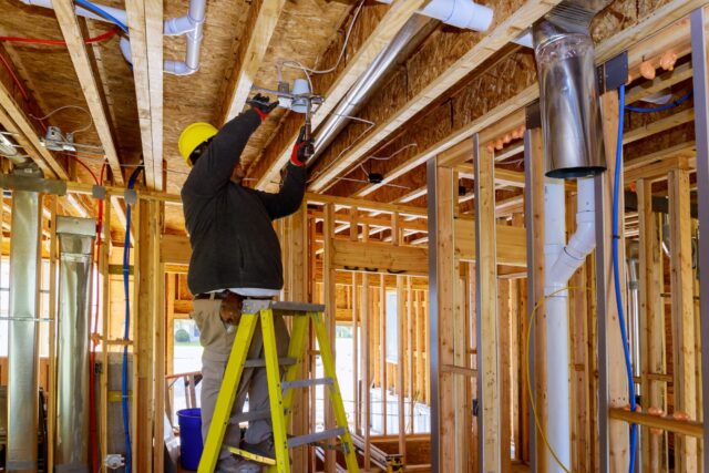 An electrician installs a lighting fixture in a building space that is under constructions.